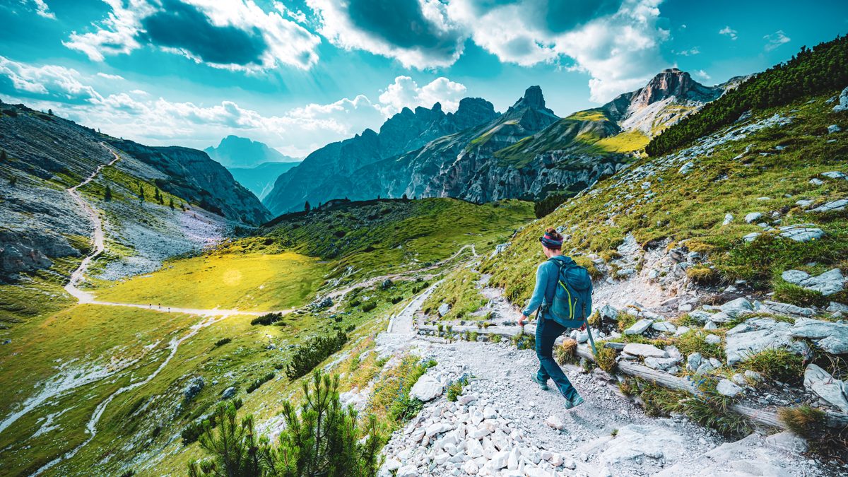A backpacker walking along a rocky Dolomites trail with mountain peaks ahead.