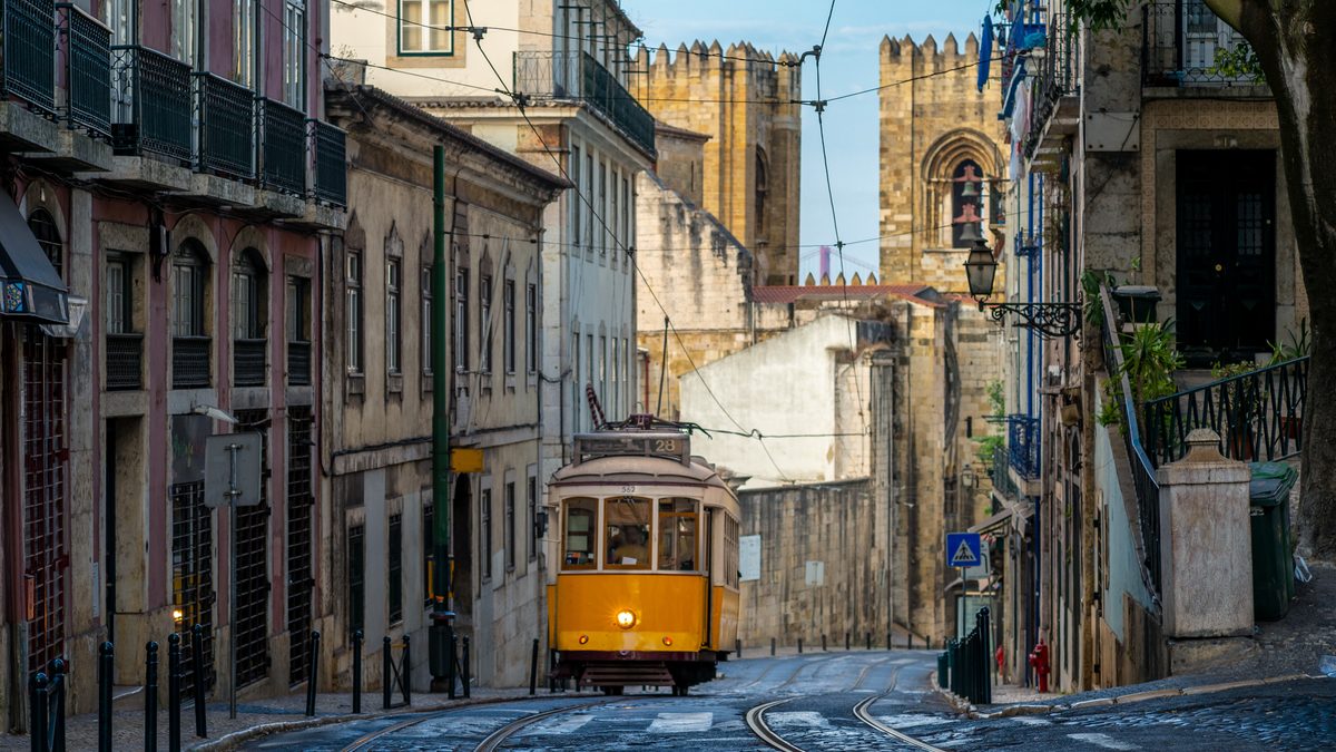 A yellow tram on a cobbled Lisbon street beside the cathedral.