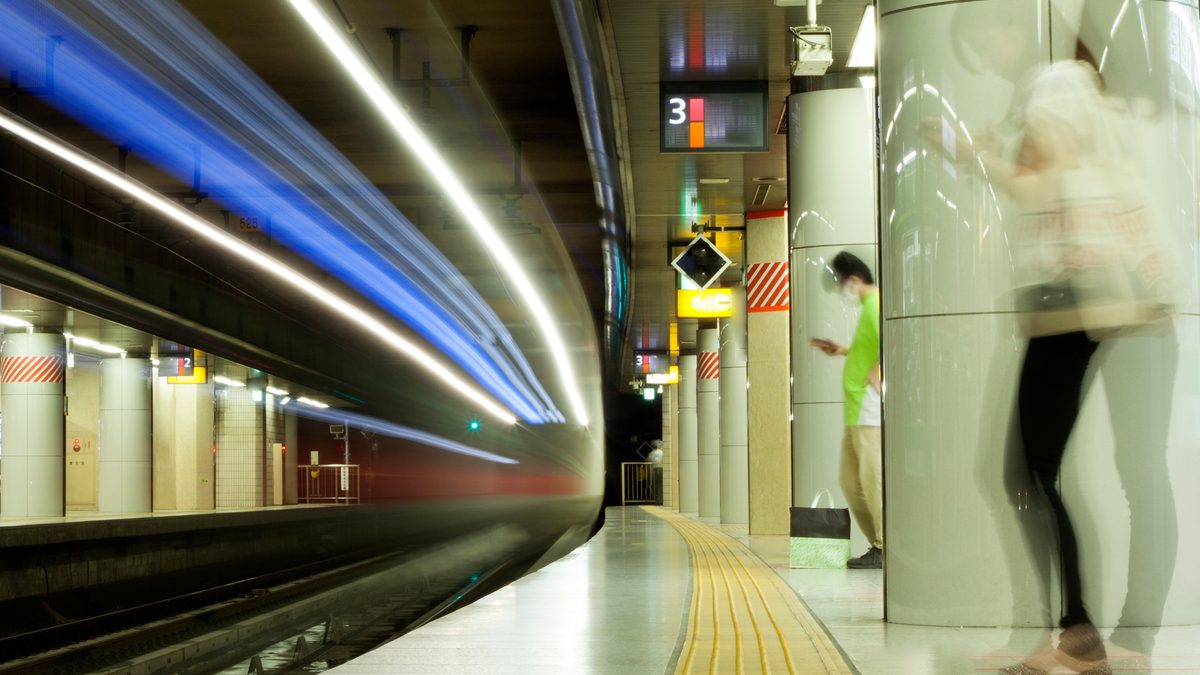 A train passing through a Tokyo station, with motion-blurred passengers on the platform.