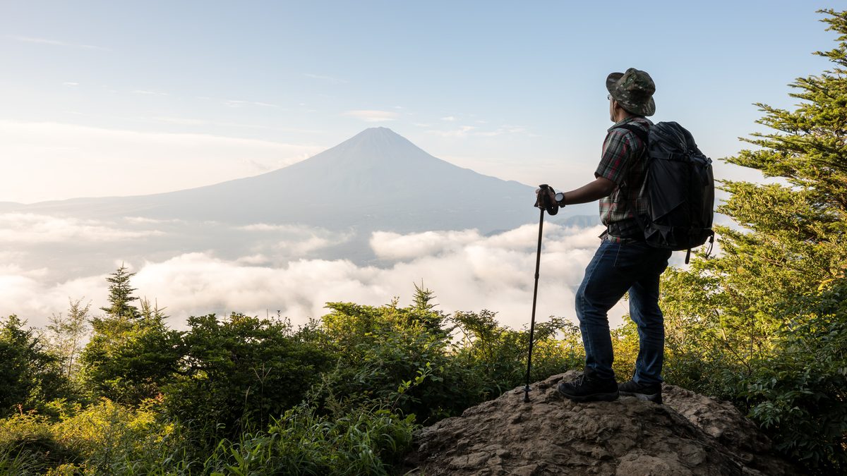 A hiker seen from behind looking towards Mount Fuji above the clouds.
