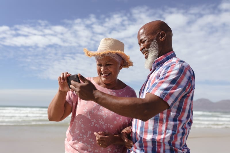 An older couple enjoying a phone together by the sea.