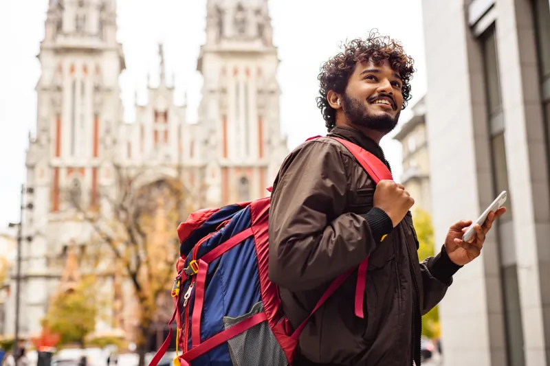 Smiling traveller with a backpack and phone exploring the city